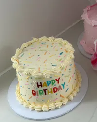 A cream birthday cake with rainbow sprinkles and Happy Birthday in coloured letters