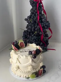 An Eid cake topped with figs and berries beside a tall tower of grapes tied with a red ribbon