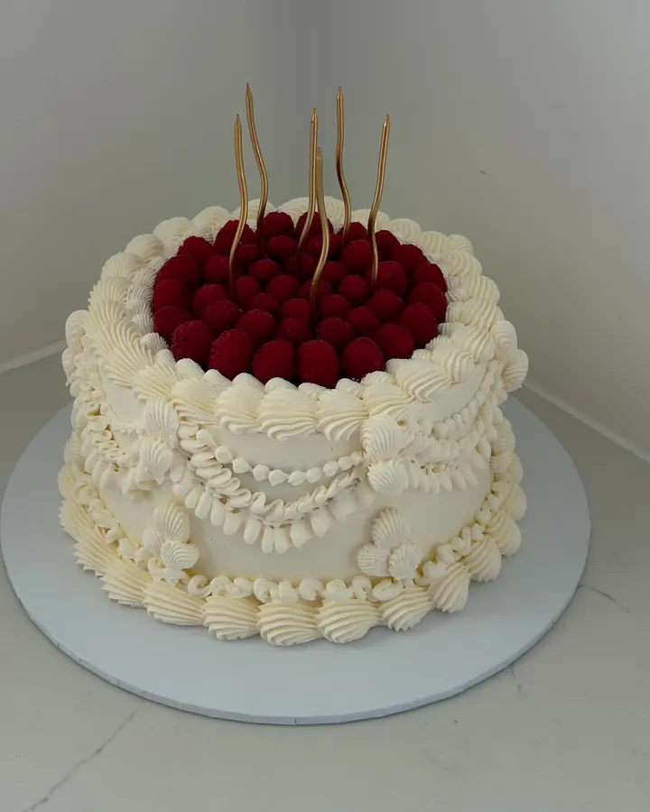 Cream vintage cake with swags of piping, piled with red berries and tall gold wavy candles