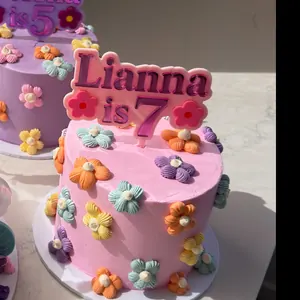Pink cake covered in piped flowers with a Lianna is 7 topper