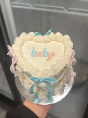 White heart mini cake reading ‘baby’ in pink and blue with pink and blue bows