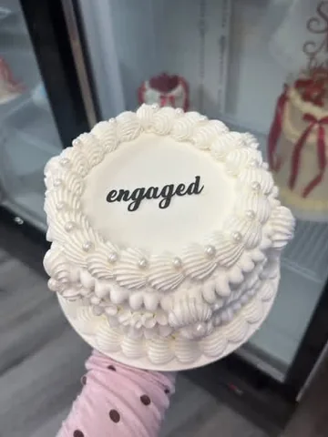 White mini cake reading ‘engaged’ with piped shells and pearls
