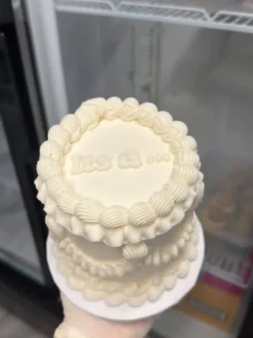 Ivory mini cake with shell piping, reading It’s a... in white piping
