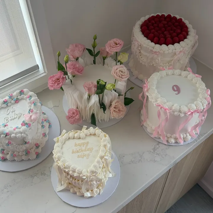 Finished cakes on a bench: a flower cake, a raspberry vintage cake, a pink number 9 cake with bows and a white heart cake
