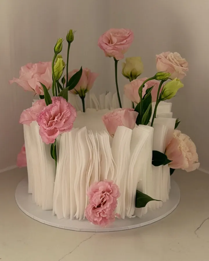 White cake wrapped in tall wafer paper ruffles, topped with fresh pink lisianthus and carnations